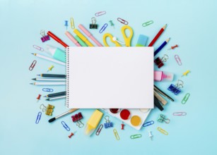 Notebook with stationary objects on blue background. Empty white paper sheet of notepad or