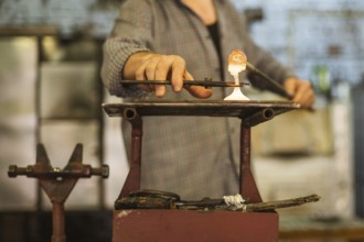 The worker makes a glass ornament in a glass smelter