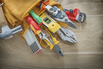 Construction tools in leather toolbelt on wood board