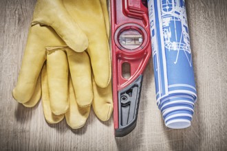 Safety leather gloves construction level blueprints on wooden board