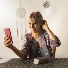 Smiling tarot reader holding her phone in hand while looking at the camera