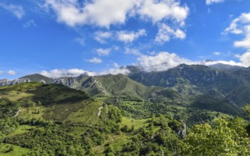 Scenic view of green hills and mountains under a bright blue sky with scattered clouds