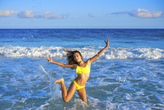 Bikini teen girl jumping happyt in Caribbean sunset beach splashing shore