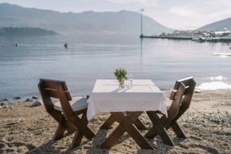 Laid table for two with chairs stands on a sandy beach by the sea.
