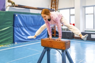 Female student performing gymnastic exercises on pommel horse during physical education class in