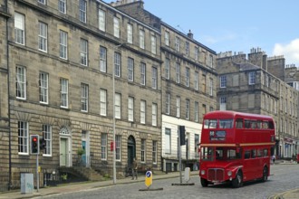 Red double-decker bus in historic old town with classic buildings and blue sky, Capital City,