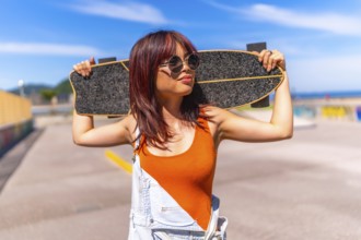 Portrait of a urban confident asian woman holding a skateboard on shoulders standing in an urban