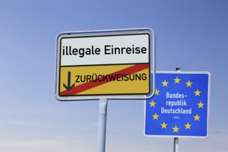 (Photomontage) Town exit sign with the inscription ILLEGAL ENTRY / REFUSAL in front of a border