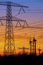 High-voltage electricity pylons, transmission towers and wind turbines at sunset near the Borssele