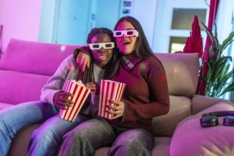 Two girls wearing 3d glasses enjoying a movie night at home, eating popcorn from striped boxes and