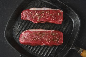 Top view of two thick cuts of raw beef steaks on a cast iron skillet. The marbled texture of the