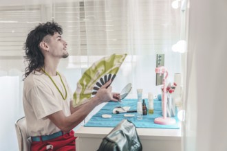 Young influencer with mullet hairstyle is cooling himself with a hand fan while applying makeup in