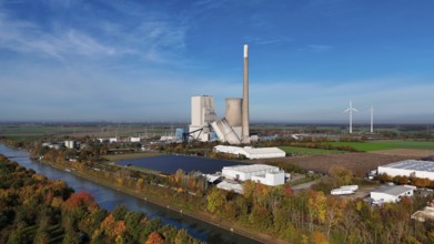 Industrial landscape with power plant and wind turbines, surrounded by autumn trees along a canal,