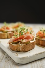 Open-faced sandwiches are arranged on a wooden platter, featuring layers of smoked salmon, pickles,