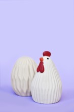 Ceramic Easter chicken and egg decoration objects on purple background with copy space