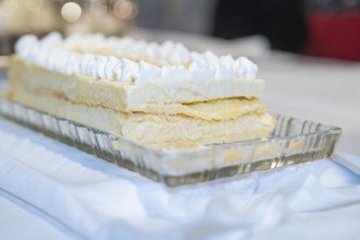A creamy layer cake on a glass dish, placed on a white table, Europäischer Hof, Königsbach Stein,