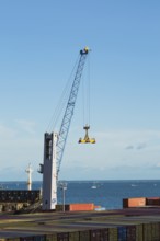Gotwald crane with lifting attachment and stacked rectangular metal box shipping conatiners on dock