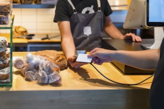Customer in the bakery shop buying an artisan bread from the baker in the workshop, paying with the