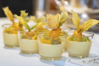 Small glasses with an exotic dessert of mango, kiwi and physalis on a white tablecloth,