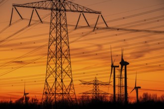 High-voltage electricity pylons, transmission towers and wind turbines at sunset near the Borssele