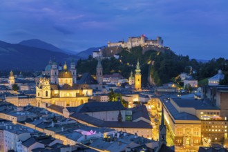 The city of Salzburg glows at dusk, dominated by the Hohensalzburg Fortress and the Alps, Salzburg,
