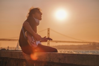 Hipster street musician in black playing electric guitar in the street on sunset