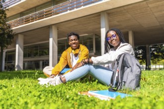 Portrait of two african university students relaxed on the grass of the campus smiling at camera