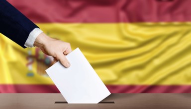 Hand holding ballot in the ballot box with the flag of Spain in the background. Spain general