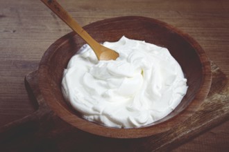 Sour cream in a wooden bowl, on a wooden table, top view, close-up, no people