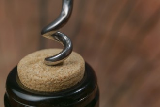 Metal corkscrew twisting into a cork in a wine bottle, ready to be opened