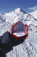 Female hand closeup holding an engagement ring inside a red heart shaped box over the snowy
