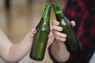 A close-up on the hands of two people. Each of them is holding a green bottle without a label. The