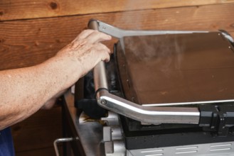 Senior hand closing metal electric grill, smoke coming up from grilled food inside, Pribylina,