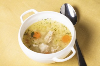 A chicken broth in white ware on the yellow tablecloth