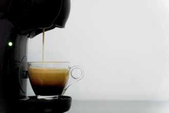 Black electric coffee maker making an espresso on a white background