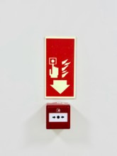 A red fire alarm button with an instructional sign above it on a white wall