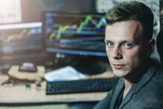 A man in an office setting with multiple monitors displaying graphs, suggesting a business