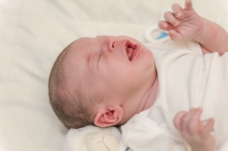 Newborn baby crying, close-up of baby lying in bed