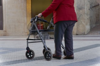 Elderly woman walking along a pedestrian street leaning on her wheeled walker