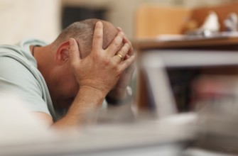 Worried businessman sitting in front of his computer with his head in his hands