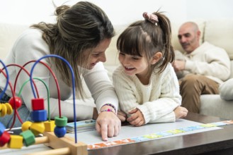 Happy family playing with alphabet puzzle, mother teaching daughter letters, father watching them,