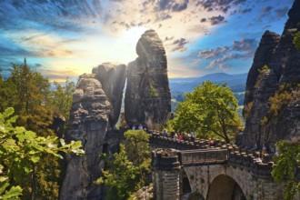 Stone Bastei Bridge connects imposing rocks at sunset, surrounded by lush trees, Elbe Sandstone