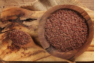 Natural, red rice, in a wooden bowl and spoon on a wooden surface in rustic style, top view