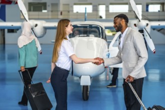 Female pilot shaking hands with businessman inside an aircraft hangar, greeting a passenger before