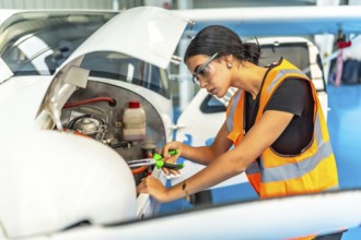 Young woman aircraft mechanic wearing safety glasses and high visibility vest using pliers while