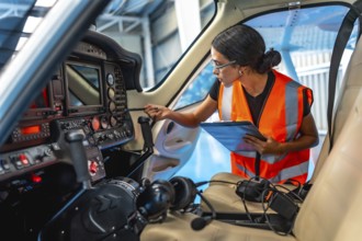Female aircraft maintenance engineer using checklist while inspecting control panel inside cockpit