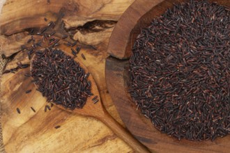 Natural black rice in a wooden bowl and spoon on a wooden surface in rustic style, top view