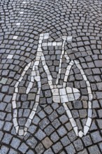 A bicycle mosaic is skilfully integrated into a street of paving stones, traffic, bicycle road,