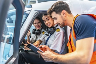 Airplane maintenance engineer briefing two smiling female pilots showing thumbs up sitting inside