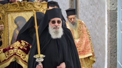 A priest in a black robe carries a candle next to an icon during a religious procession, Orthodox